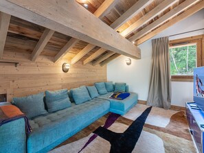 A cozy room with a large sectional sofa, wooden beams, a window with curtains, and a rug.