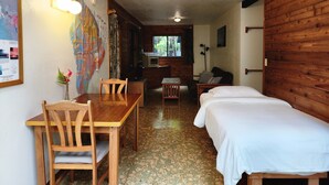 A room with two beds, a wooden table, chairs, a map on the wall, and a small kitchenette. - The Pacifica Inn/ 
The Gecko Room (Volcano)