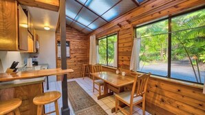 A wooden cabin with a dining area, kitchen, and large windows offering a view of the outdoors. - The Pacifica Inn/ 
The Gecko Room (Volcano)