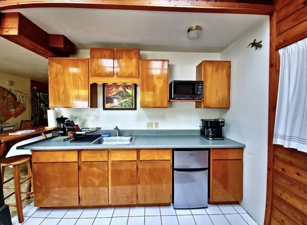 A compact kitchen with wooden cabinets, a built-in microwave, a sink, and a refrigerator.