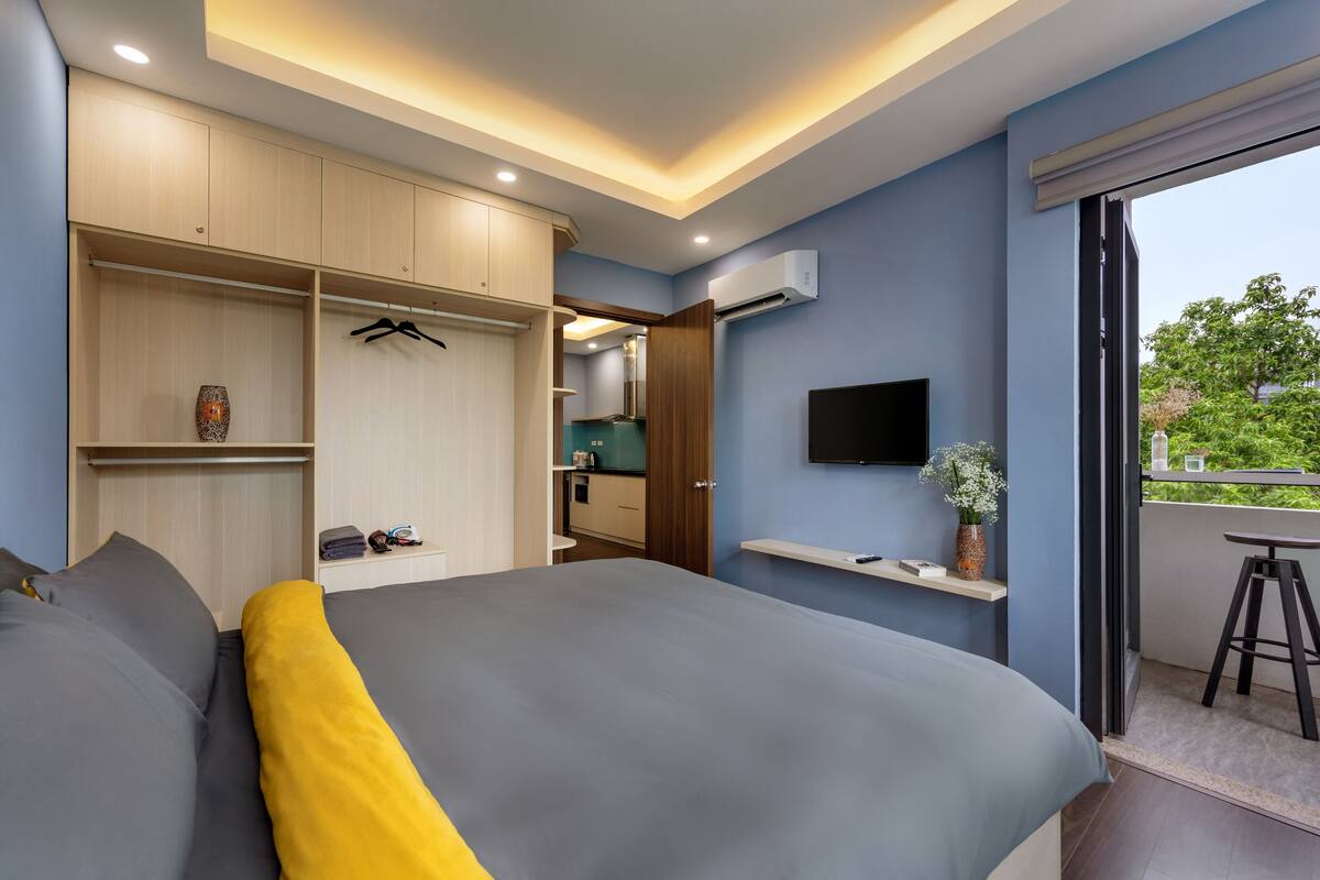 A modern bedroom with a large bed, built-in wardrobe, and a balcony with a view.