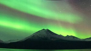 A mountain range with a reflection in a body of water under a green aurora.
