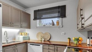 A modern kitchen with wooden cabinets, a dishwasher, a window with a blind, and a wooden countertop.