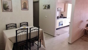 Een eethoek met een tafel en stoelen, een keuken op de achtergrond en een deur naar een andere kamer.