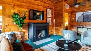 A cozy cabin interior with a fireplace, wooden walls, a television, and comfortable seating. - Serene Cabin, Sleeps 12 W Views・Hot tub・Games (Sevierville)