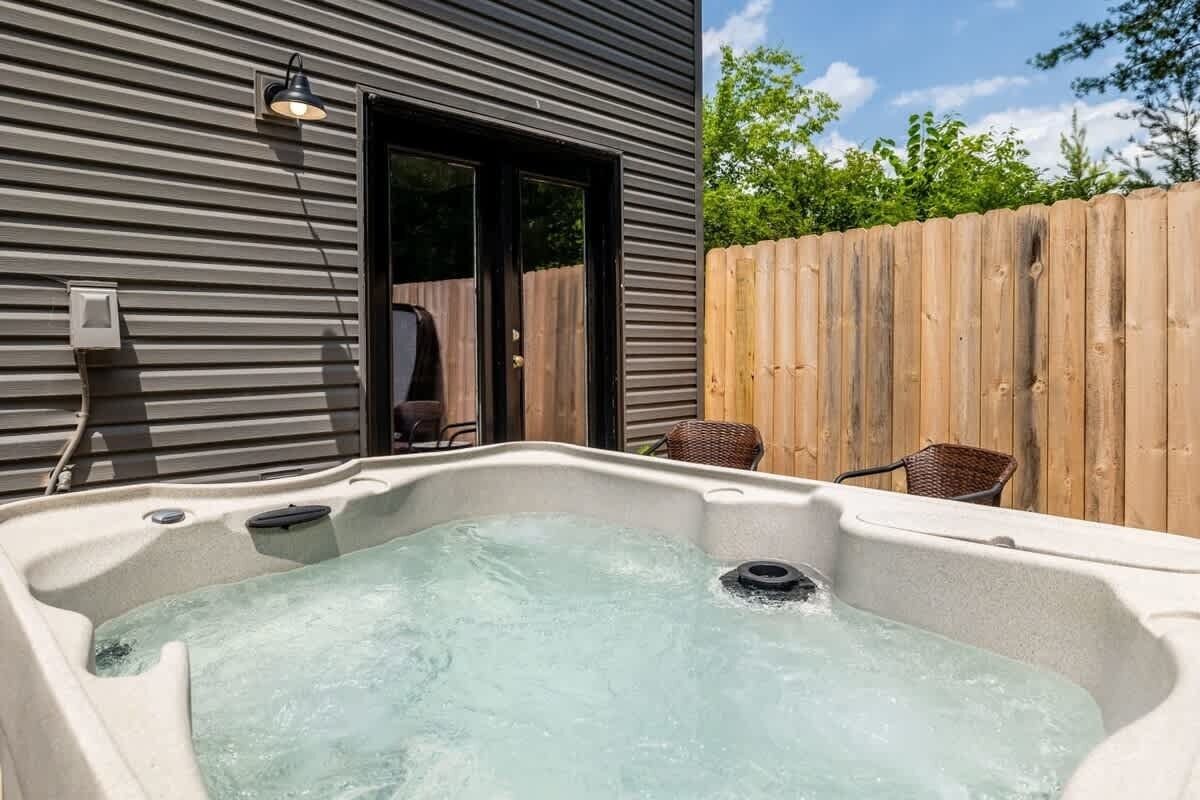A hot tub in a backyard with a wooden fence and a house in the background.