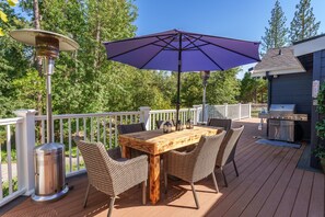Eine Terrassenanlage mit Holztisch, Korbstühlen, einem Grill und Sonnenschirm.