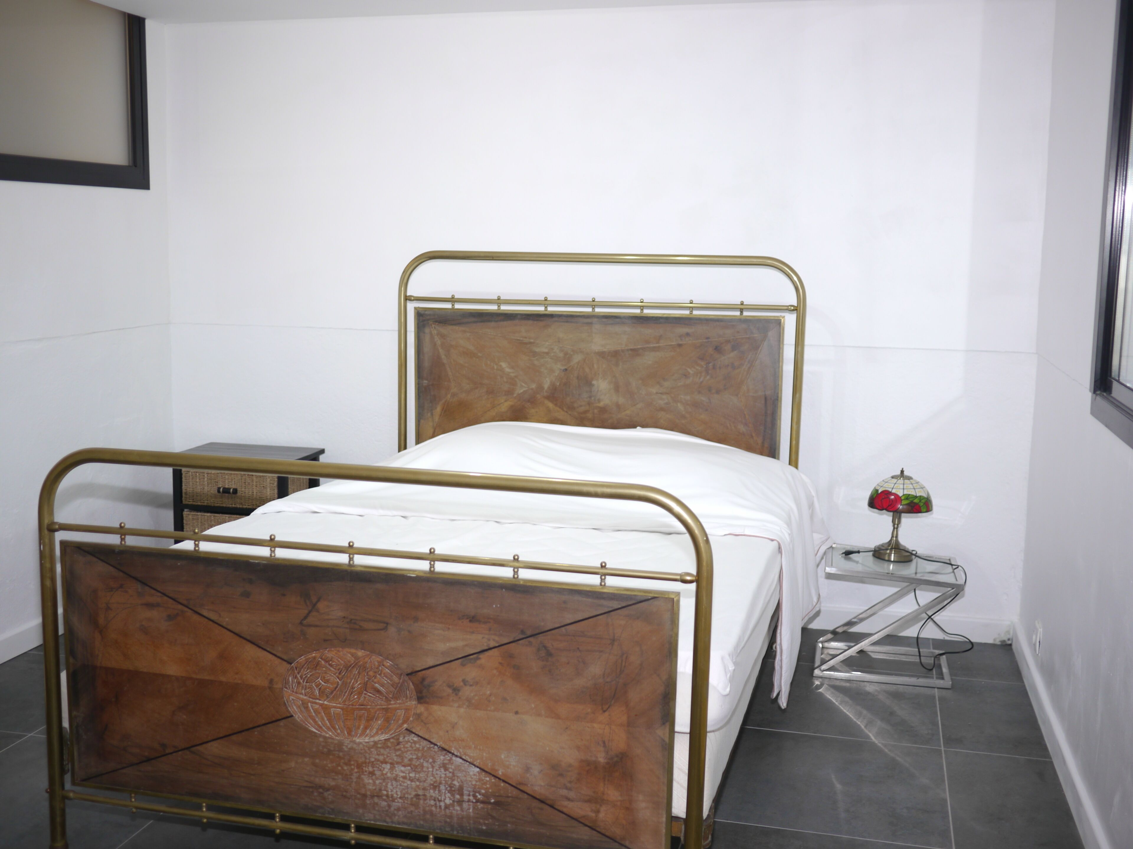 A single bed with a metal frame and wooden headboard in a room with white walls and tiled floor.