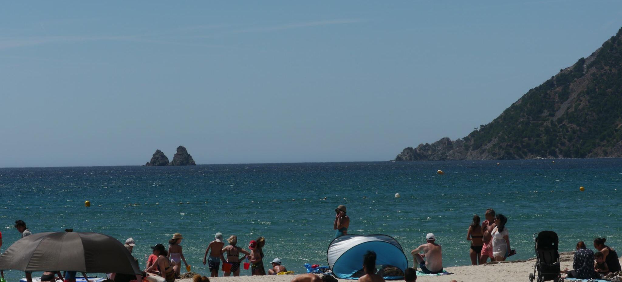 Una playa con gente, tiendas de campaña y un litoral rocoso.