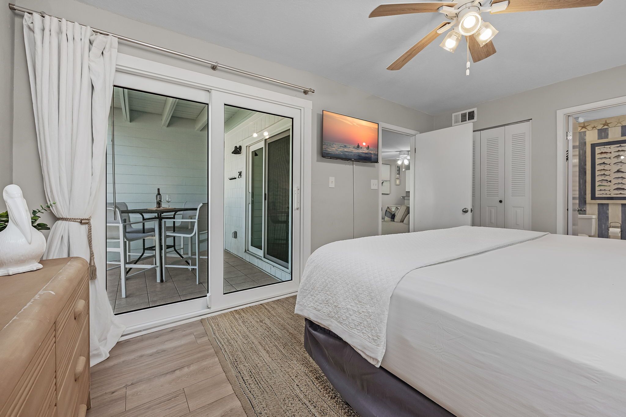A bedroom with a bed, a ceiling fan, a TV, and a sliding glass door leading to a balcony.