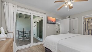 A bedroom with a bed, a ceiling fan, a TV, and a sliding glass door leading to a balcony. - Tradewinds 24 * Across from the beach * Fall Rates * Salt Water Vacations (Miramar Beach)
