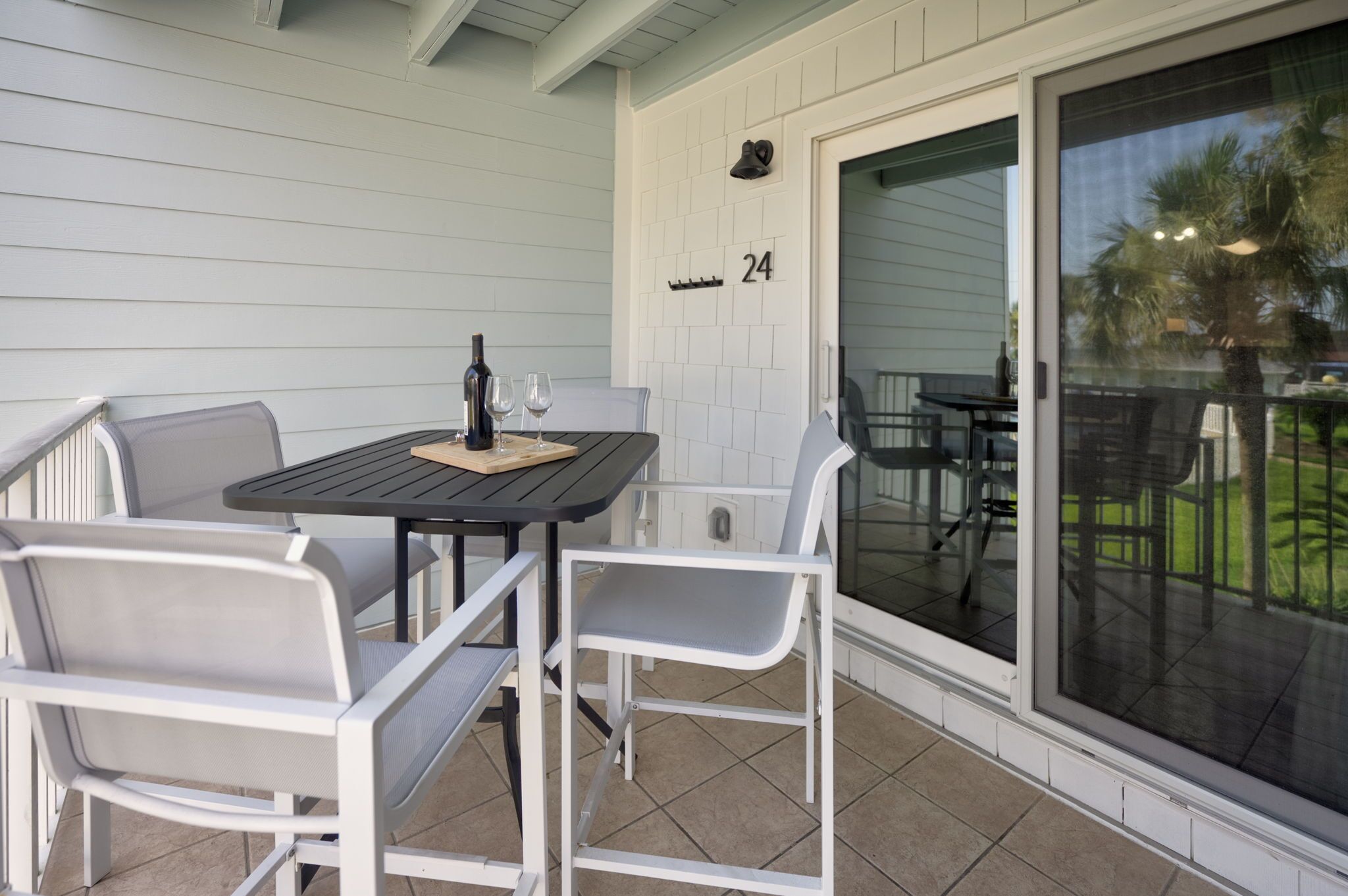 A covered patio area with a table and chairs, a bottle of wine, and a number '24' on the wall.