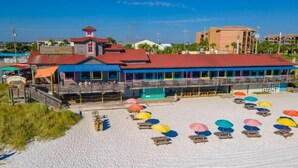 A beachside building with a red roof, a covered seating area, and multiple colorful umbrellas on the sand. - Tradewinds 24 * Across from the beach * Fall Rates * Salt Water Vacations (Miramar Beach)