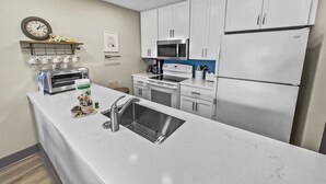 A modern kitchen with white cabinets, a stainless steel refrigerator, a microwave, a stove, and a sink. - Tradewinds 26 * Across from the beach * Fall Rates * Salt Water Vacations (Miramar Beach)