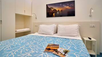 Ein Hotelzimmer mit einem großen Bett, einem Nachttisch, einem Wandbild mit Sonnenuntergang und einer Ablage mit einem gefalteten Handtuch.