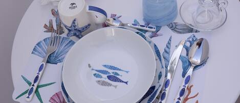 Uma mesa posta com pratos brancos, estampas de peixes em azul e vermelho, e talheres.