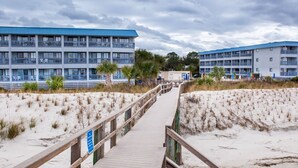 A wooden boardwalk leading to a beachfront hotel with multiple balconies and a sandy beach. - Breezy Palms on the Bay!  Dolphins, Pools, Beach (Tybee Island)