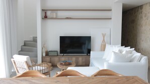 Ein modernes Wohnzimmer mit einem weißen Sofa, Holzstühlen, einem Fernseher und einem Esstisch.