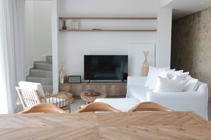Un salon moderne avec un canapé blanc, des chaises en bois, un téléviseur et une table à manger.