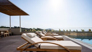 Ein Poolbereich mit Liegestühlen und einem Tisch, mit Blick auf einen Pool und eine entfernte Landschaft.