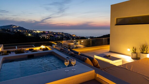 Eine Dachterrasse mit Whirlpool, Sitzgelegenheiten und Blick auf die Stadt im Abendlicht.
