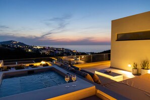 A rooftop terrace with a hot tub, seating area, and a view of the city at dusk.