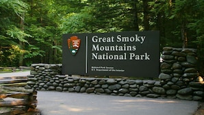 Schild für den Great Smoky Mountains National Park, mit einer Steinmauer und bewaldetem Hintergrund.