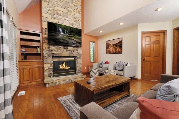 A living room with a stone fireplace, a television mounted above it, and a cozy seating area with a coffee table. - Gateway to the Smokies: Your Door to the Mountains (Pigeon Forge)