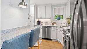 A modern kitchen with white cabinets, stainless steel appliances, and a marble countertop. - Shore Cottage - Coastal gem, a traveler favorite! Outdoor patio, central AC. (Gloucester)
