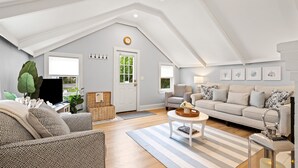 A spacious living room with a high ceiling, a sofa set, a coffee table, and a television. - Shore Cottage - Coastal gem, a traveler favorite! Outdoor patio, central AC. (Gloucester)