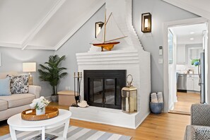 A living room with a fireplace, a sofa, a coffee table, and a potted plant. - Shore Cottage - Coastal gem, a traveler favorite! Outdoor patio, central AC. (Gloucester)