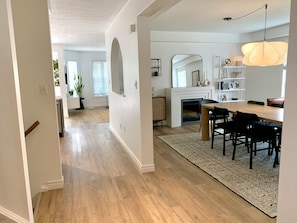Un vaste espace de vie doté d’un plancher en bois, d’une table à manger avec des chaises, d’une cheminée et d’un grand miroir mural.