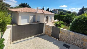 Uma casa de dois andares com telhado em telhas, varanda coberta e muro de pedra.