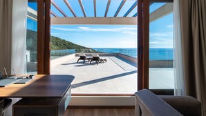A modern room with a large sliding glass door leading to a balcony with a view of the sea and a hilly landscape. - Cape Montenegro Villas (Krimovica)