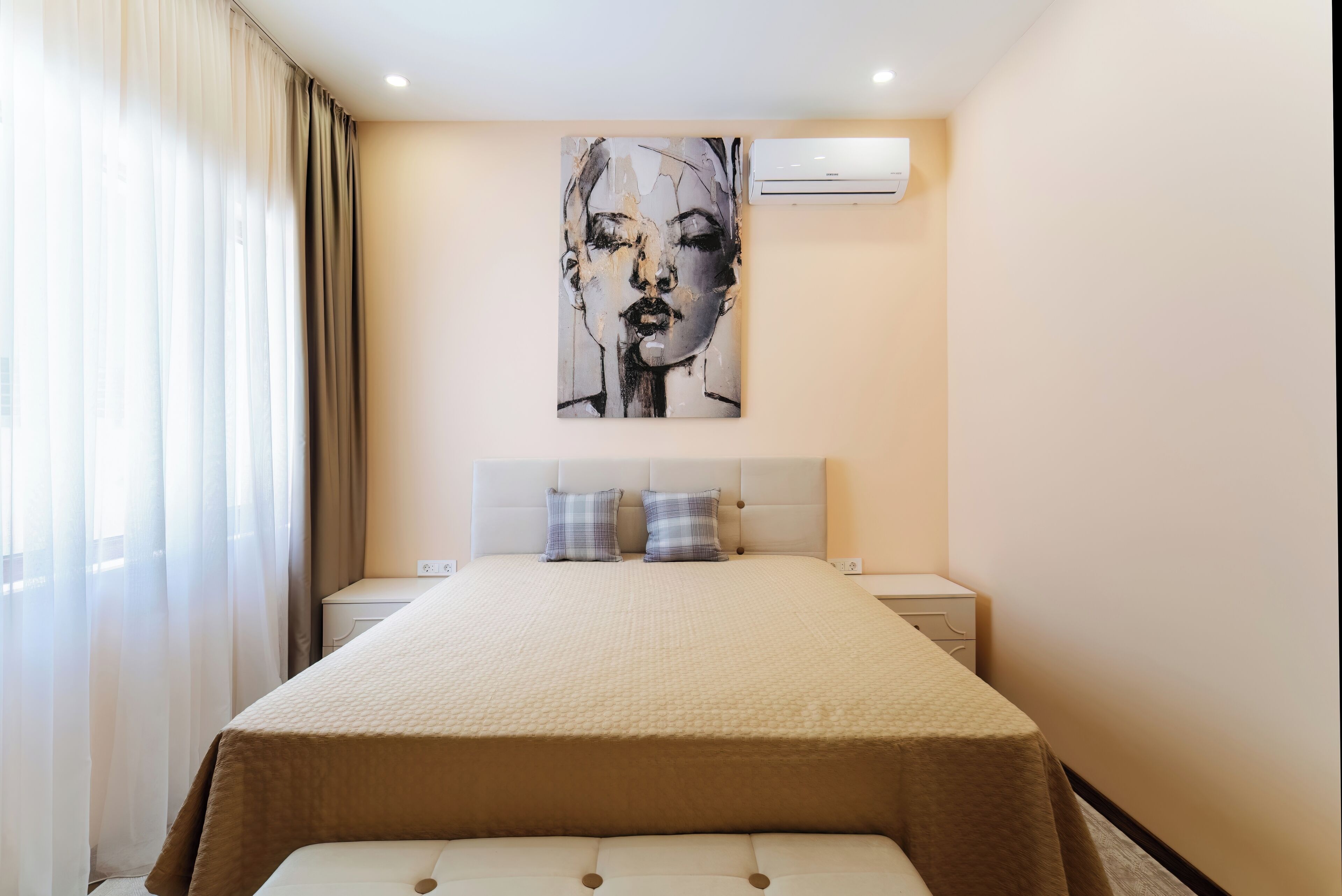 A hotel room with a large bed, a headboard, two bedside tables, and an air conditioning unit on the wall.