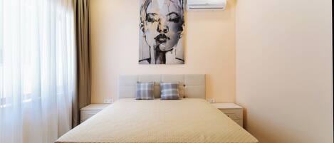 A hotel room with a large bed, a headboard, two bedside tables, and an air conditioning unit on the wall.