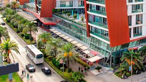 A modern hotel with a distinctive red and white facade, multiple floors, and a covered outdoor area with seating. - Cape Montenegro Villas (Krimovica)