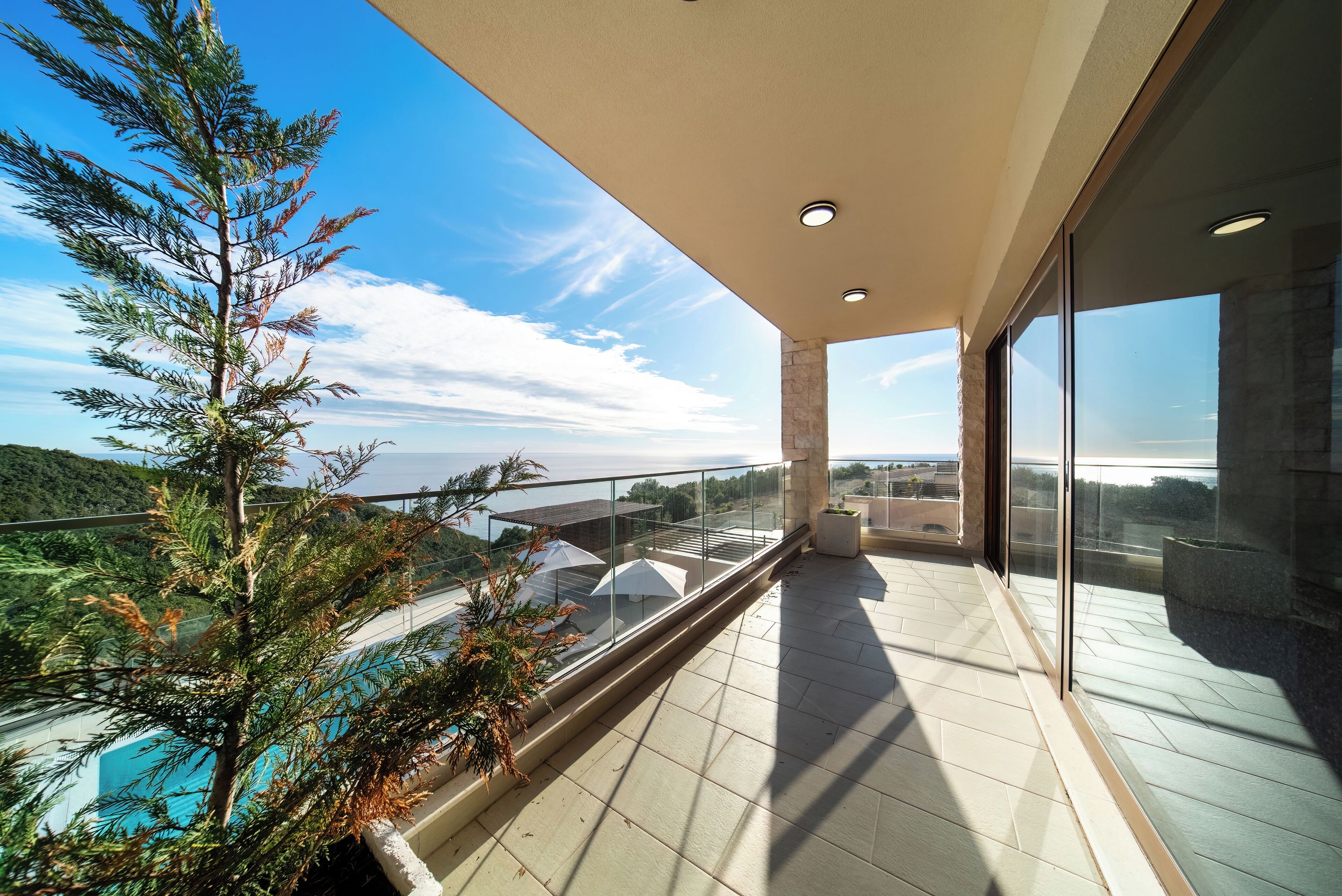 A balcony with a glass railing overlooking a pool and a mountainous landscape.