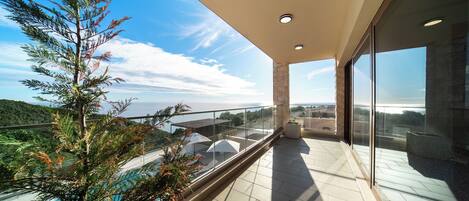 A balcony with a glass railing overlooking a pool and a mountainous landscape.