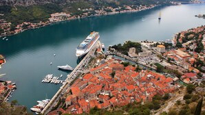 A cruise ship docked at a port with red-roofed buildings and a mountainous backdrop. - Cape Montenegro Villas (Krimovica)