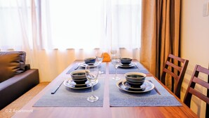 A dining table set with bowls, plates, and wine glasses, with a sofa and curtains in the background. - Near Tsutenkaku, Toy Street, Spacious,Elevator,Wi-Fi,Self check-in, Easy Transit (Osaka)
