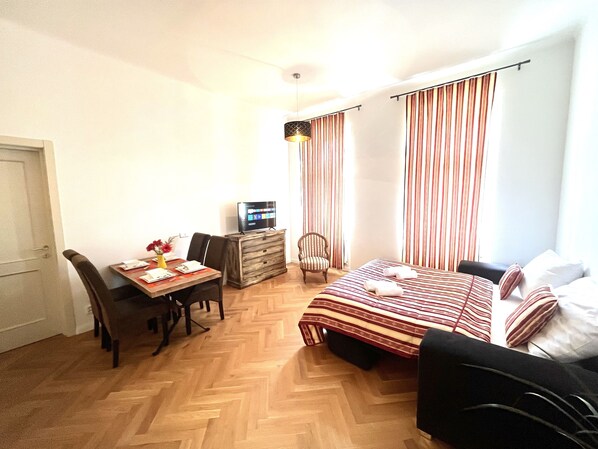 A hotel room with a bed, a desk with a computer, a chair, and a window with curtains.