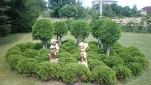A garden with neatly trimmed hedges and two statues. - Hotel Getliin (Saku)