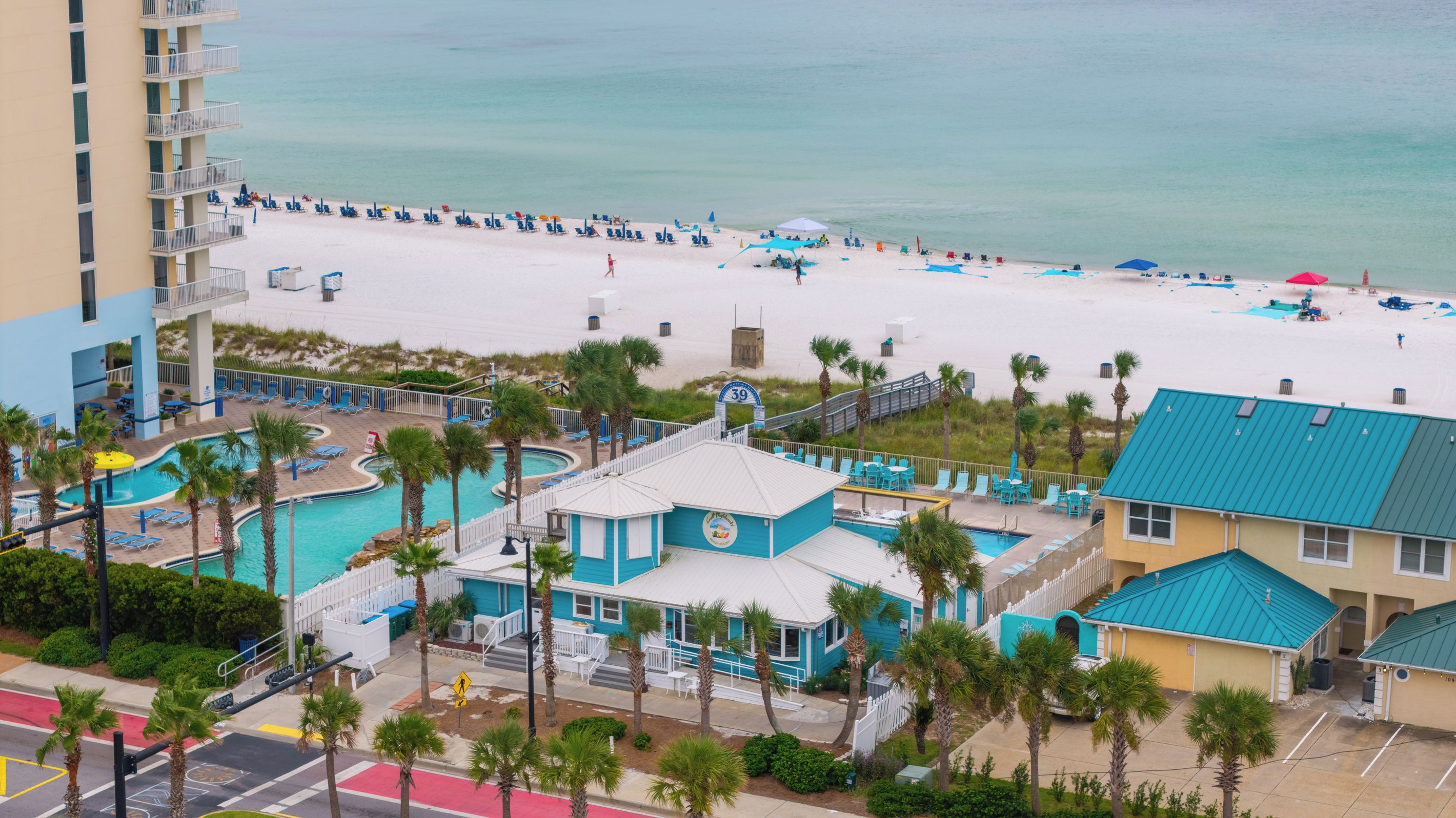 A beach resort with a swimming pool, beach chairs, and a view of the ocean.