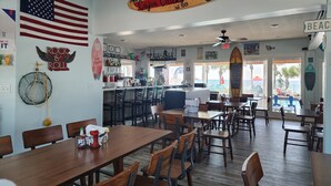 Een restaurantinterieur met een bar, verschillende zithoeken en uitzicht op het strand.