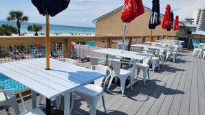 Een terras met witte tafels en stoelen, rode parasols en een zwembad.