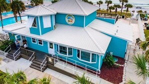 Een turquoise gebouw met uitzicht op het strand, een zwembad en een bord dat een restaurant aangeeft.