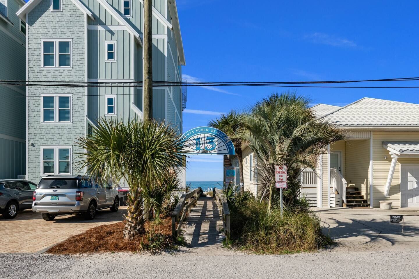 A beachfront property with a gated entrance, palm trees, and a clear view of the ocean.
