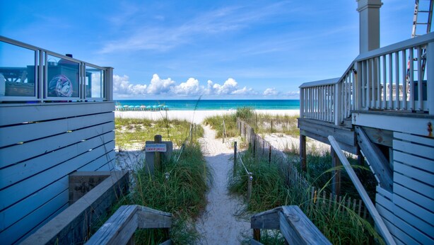 Ein Holzsteg führt zu einem Strand mit freiem Blick auf das Meer und einer Holzkonstruktion mit Geländer.
