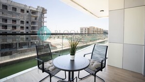 Ein Balkon mit rundem Tisch, zwei Stühlen, einem Blumentopf und Blick auf eine Baustelle.